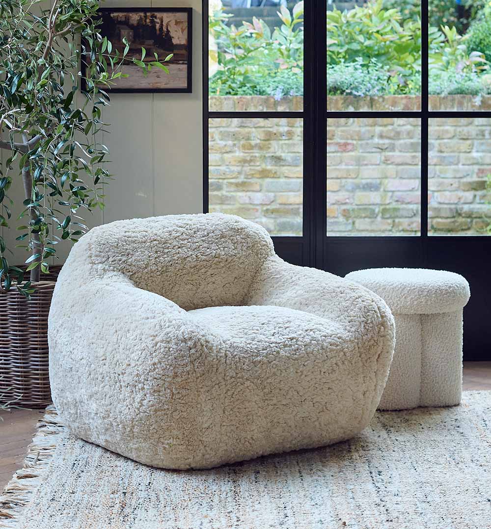 The Monroe Faux Shearling Armchair, an oversized cosy tub style chair in cream, on a neutral toned rug in a light airy room.