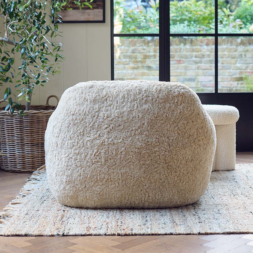 The Monroe Faux Shearling Armchair, an oversized cosy tub style chair in cream, on a neutral toned rug in a light airy room.