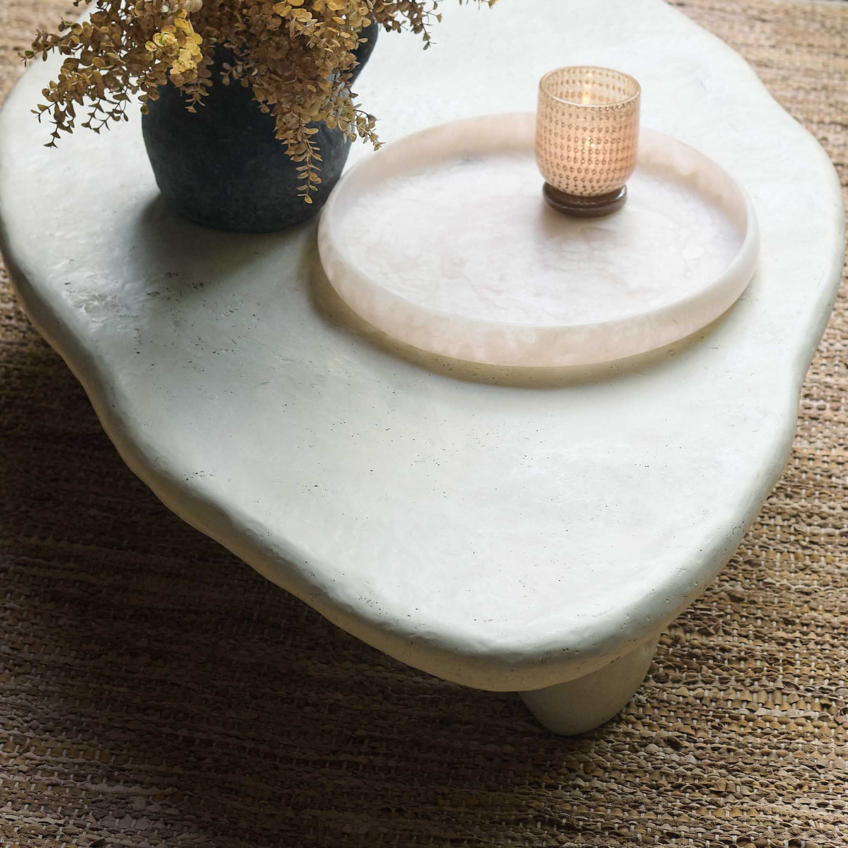 Cream stone effect coffee table with a sculptural round design, curved silhouette and textured organic finish. Medina Coffee Table by Abigail Ahern, featuring a contemporary shape and neutral tones that create an elegant centrepiece for modern living rooms and luxury interiors. A statement designer coffee table perfect for styling with decorative accessories, books and lighting, adding natural texture and timeless sophistication to your home decor.