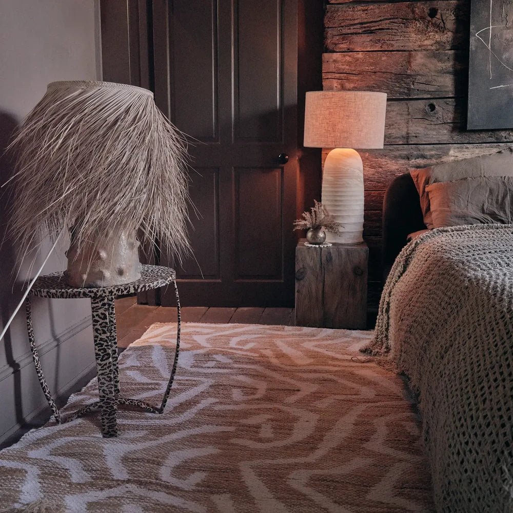 Montgomery Chenille Jute Rug spreads across a living room floor in cream and warm tan, with abstract flowing motifs beside a sofa and patterned side table.