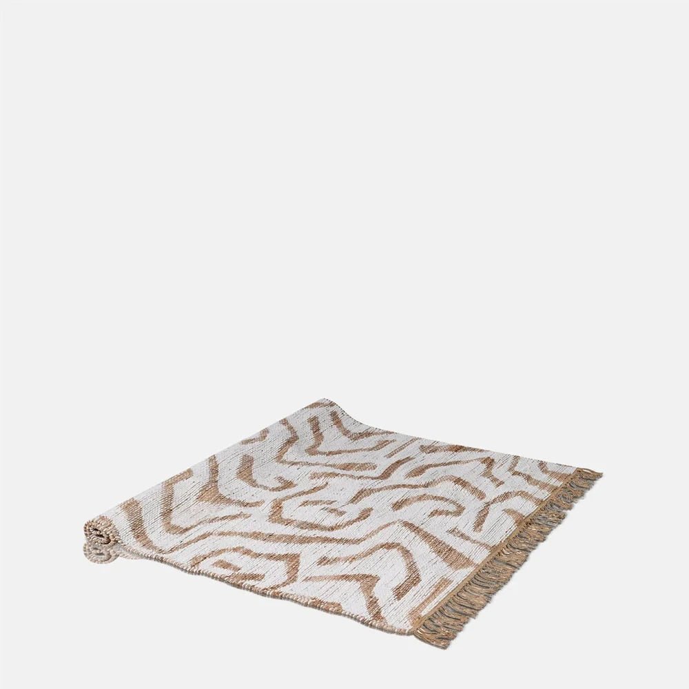Montgomery Chenille Jute Rug combines cream and tan abstract curved motifs with a textured woven surface and fringed ends, shown partly rolled at one corner.