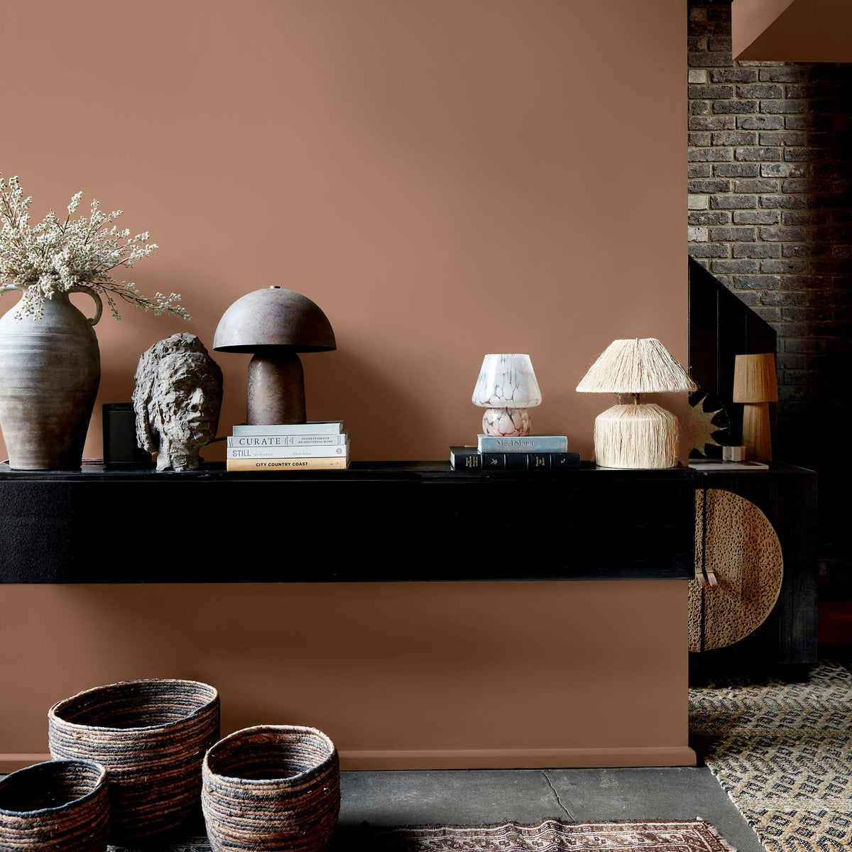 Abigail Ahern Nordic Mist paint – a sumptuous dusky pink with warm orange undertones enveloping a beautifully styled wall with mounted shelf, lamps and vases