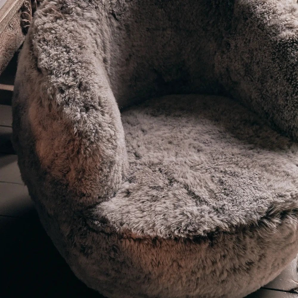 Norwood Sheepskin Swivel Chair shows its curved back and deep rounded seat in close-up, highlighting the dense grey texture across the arms and cushion.