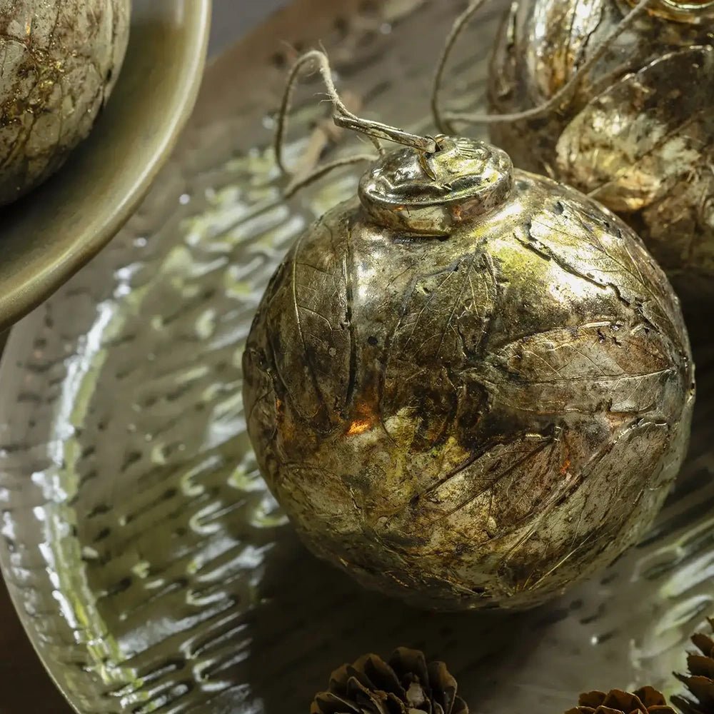 Perth antique silver leaf bauble displays textured leaf patterns across a rounded metallic surface, with its hanging loop visible beside another bauble on a decorative platter.