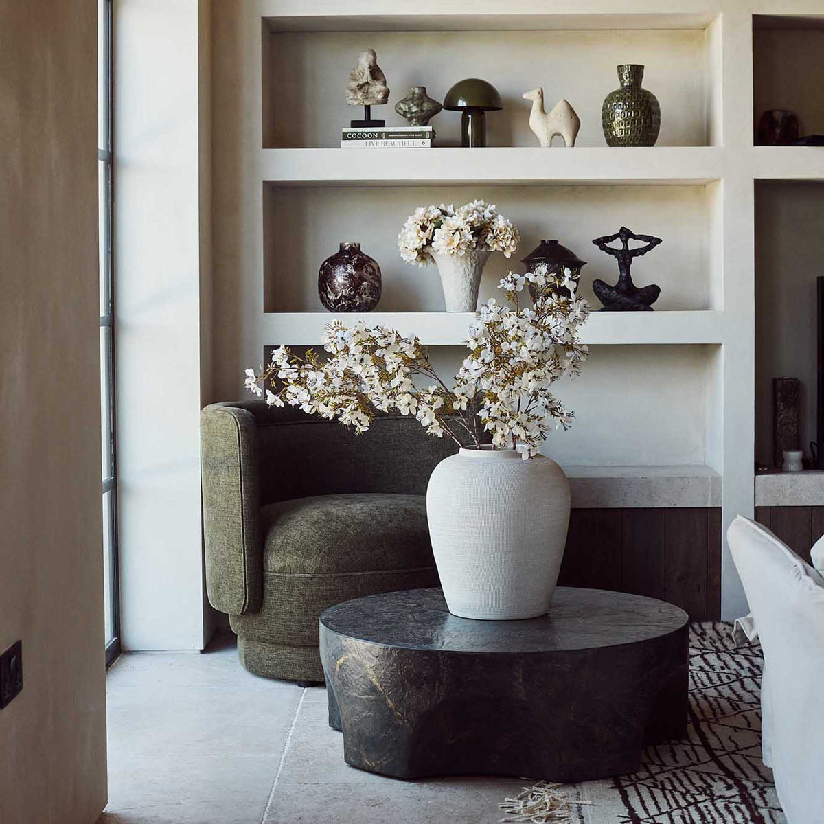 Round concrete coffee table with a sculptural pinched base and rustic brown and slate grey finish. Pinch Round Coffee Table by Abigail Ahern, crafted from glass-reinforced concrete with a textured hand-painted effect, creating a luxury statement piece for modern living rooms, contemporary interiors and stylish outdoor spaces. A unique designer coffee table that adds natural texture, character and effortless sophistication to your home decor.