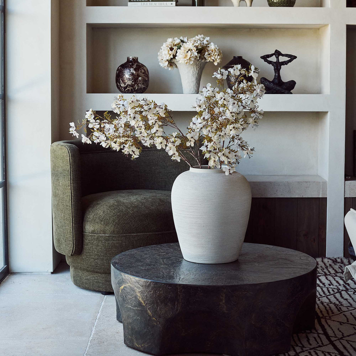 Round coffee table with a sculptural pinched base and rustic brown and slate grey finish. Pinch Round Coffee Table by Abigail Ahern, crafted from glass-reinforced concrete with a textured hand-painted effect, creating a luxury statement piece for modern living rooms, contemporary interiors and stylish outdoor spaces. A unique designer coffee table that adds natural texture, character and effortless sophistication to your home decor.