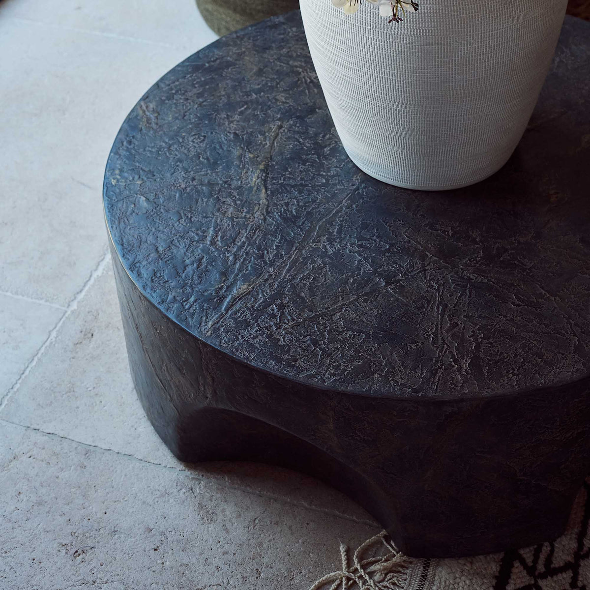 Close up of concrete coffee table with a sculptural pinched base and rustic brown and slate grey finish. Pinch Round Coffee Table by Abigail Ahern, crafted from glass-reinforced concrete with a textured hand-painted effect, creating a luxury statement piece for modern living rooms, contemporary interiors and stylish outdoor spaces. A unique designer coffee table that adds natural texture, character and effortless sophistication to your home decor.