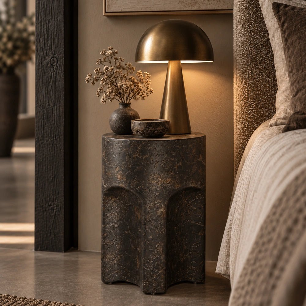Pinch Round Side Table beside a cream sofa, styled with a glowing lamp, dark ceramic vase and layered neutral furnishings in a contemporary living room.