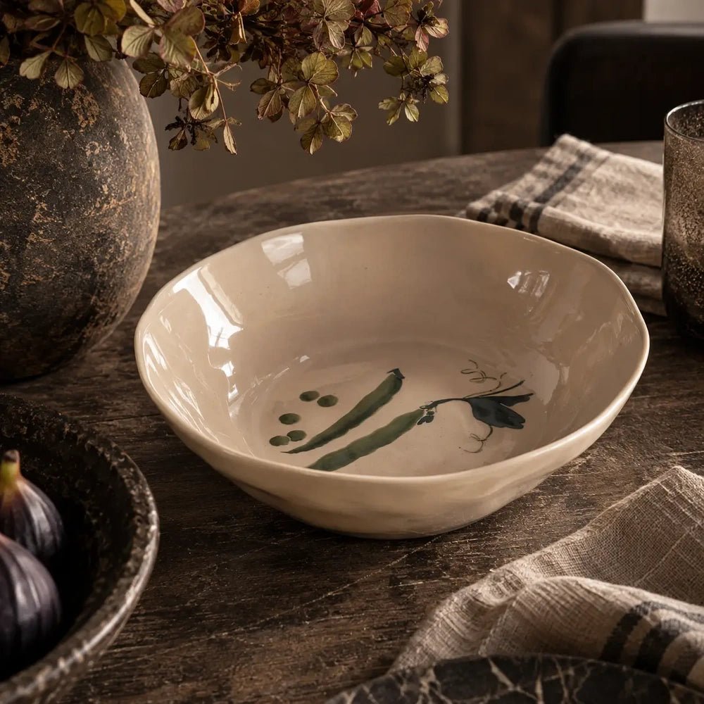 Quincy Ceramic Bowl has a shallow cream glazed form with green pea illustrations, styled on a stone console beside a textured vase and folded fabric.