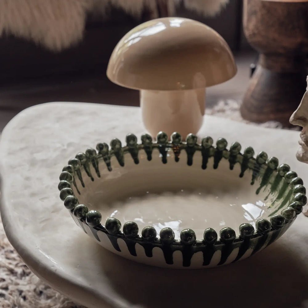 Radcliff bobble decorative bowl with a cream interior, green stripes and rounded rim details, placed on a pale coffee table beside a mushroom lamp.
