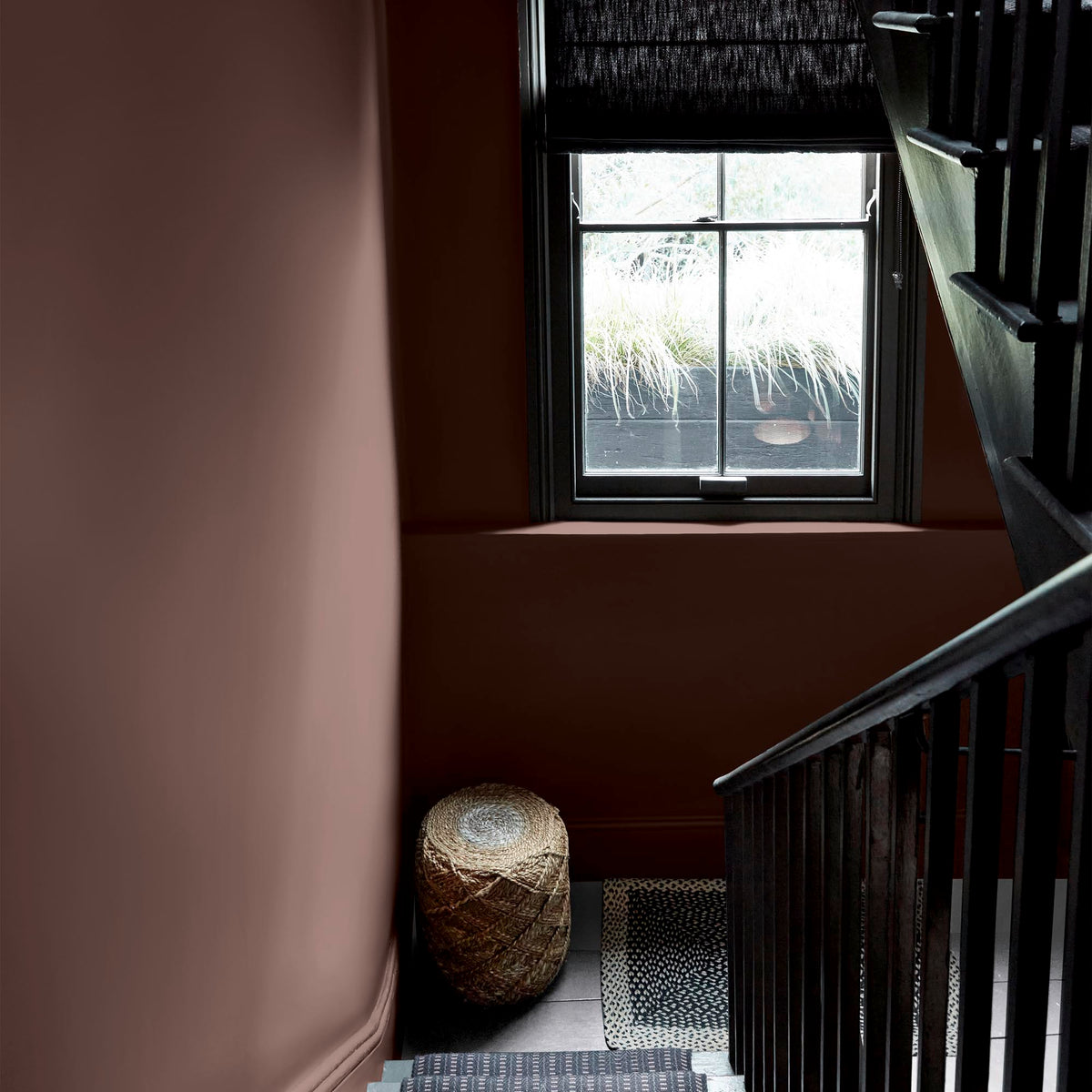 A stairway with a window with the walls painted in a warm, brown paint colour with a mauve undertone.