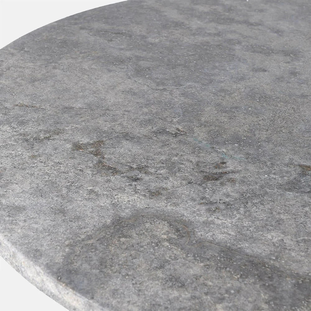 Randolph travertine dining table surface shown close up, revealing mottled grey tones, irregular stone markings and the softly rounded edge of the circular tabletop.