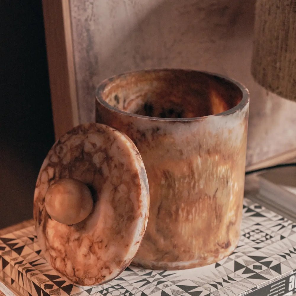 Reeve marble effect jar shown open with its lid leaning beside it, revealing the amber patterned interior and cylindrical shape on a stack of books.