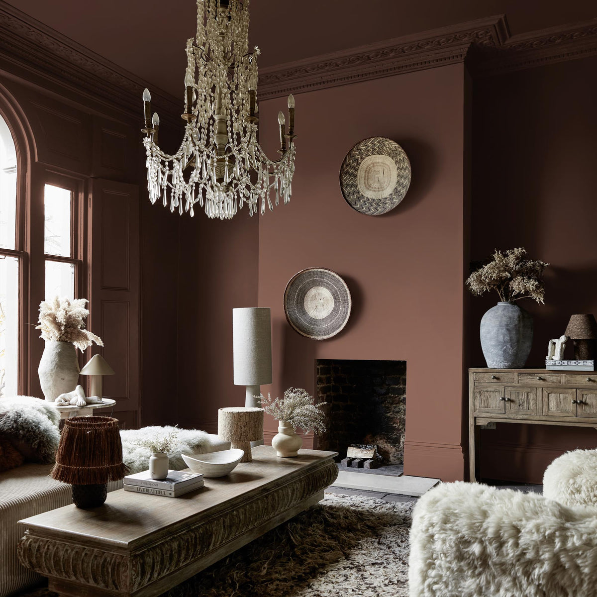 Abigail Ahern Rocky Desert paint – a sumptuous bold terracotta enveloping a beautifully styled living room beneath a statement glass chandelier
