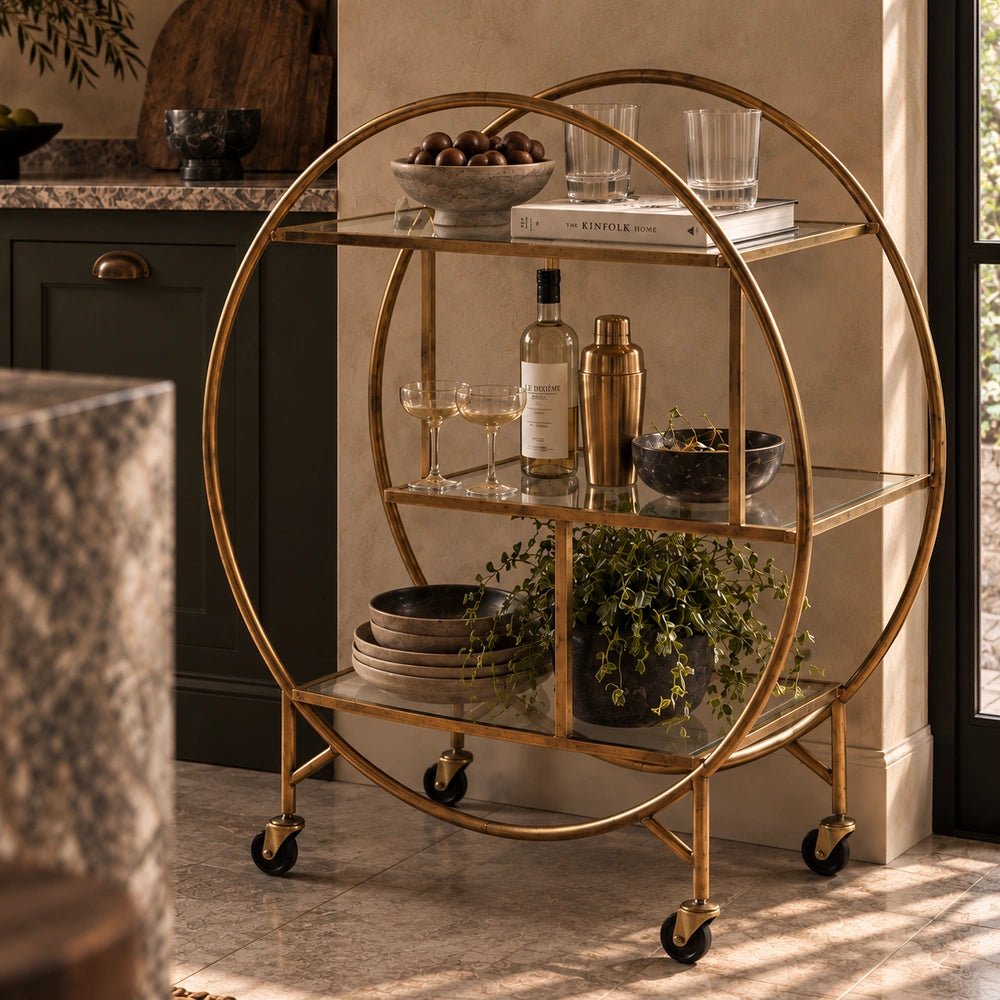 Rover Drinks Trolley with dark frame and glass shelves, styled with drinks and decorative objects in a layered contemporary living room setting.