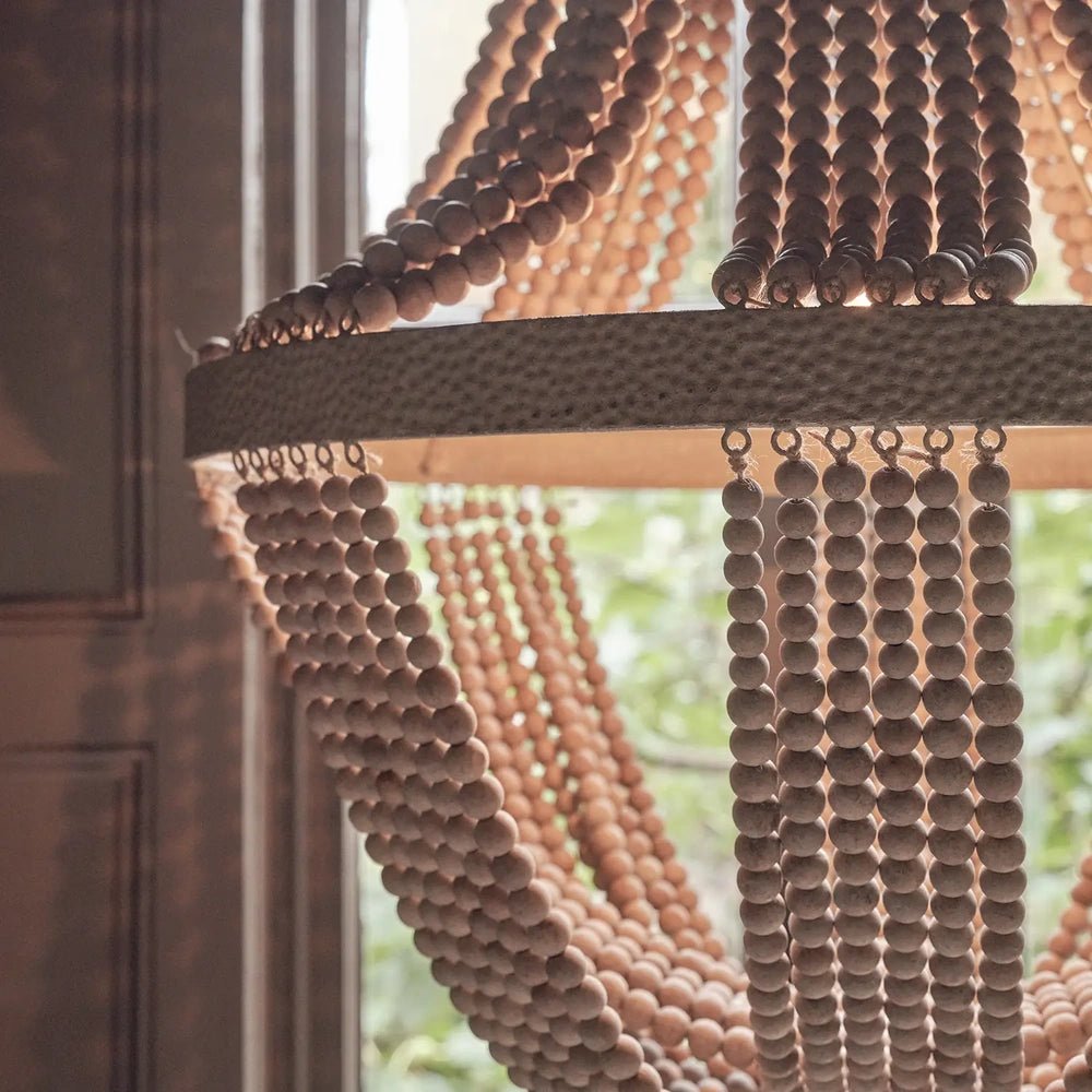 Roxham beaded chandelier shown in detail, with rounded beads forming curved strands around a broad textured band, illuminated by daylight from the window behind.