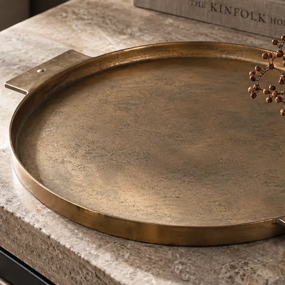 Sandford metal decorative tray shown close up, revealing its warm brass toned surface, shallow raised rim and broad rectangular handle resting on a stone tabletop.