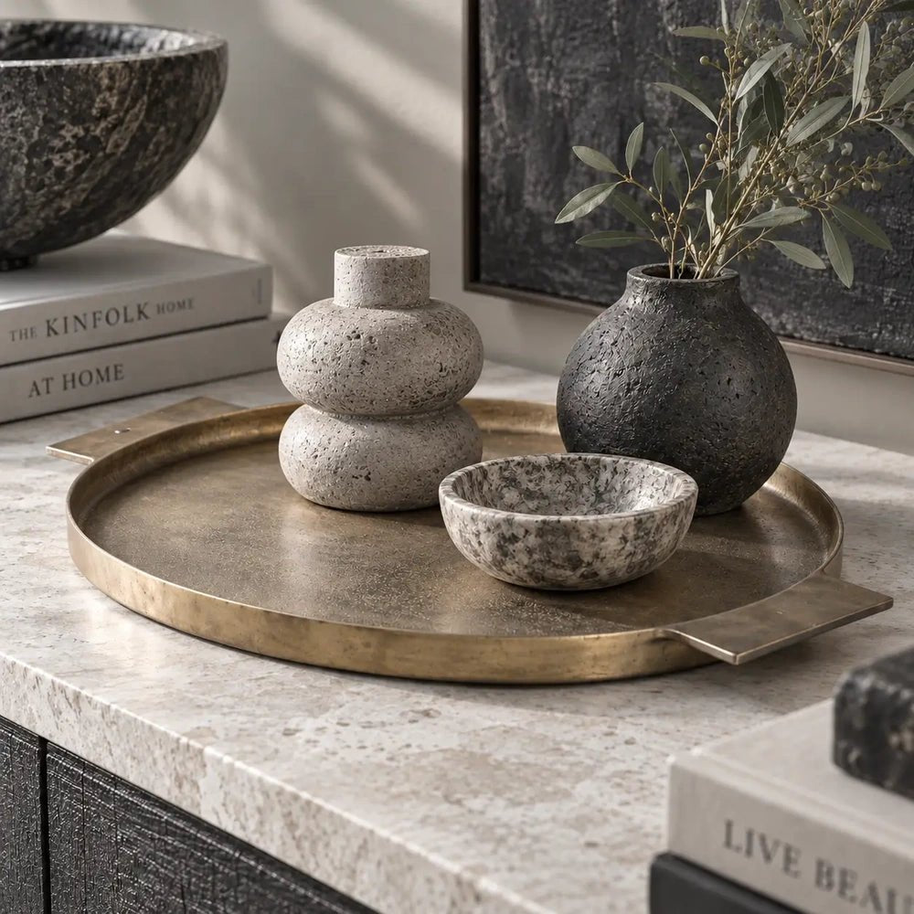 Sandford metal decorative tray with a round brass toned surface and flat rectangular handles, holding small vases and a bowl on a pale stone console.