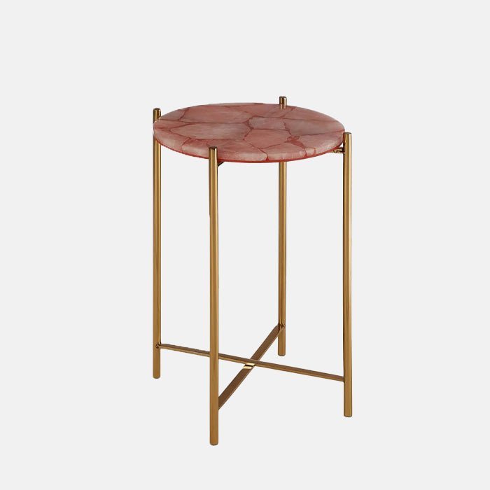 The Sandon Quartz Side Table, a small round table with a top made of solid natural quartz in a pinky hue, with slim gold legs.