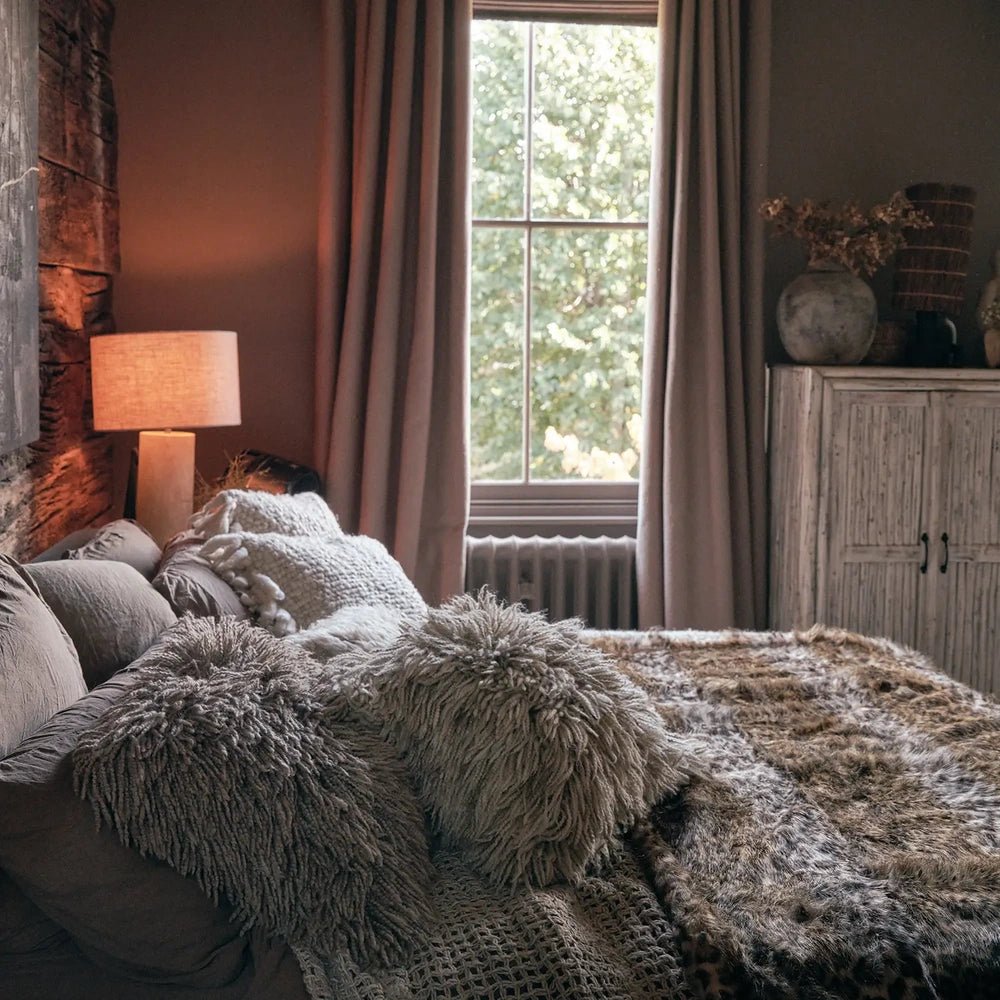 Savannah throw with a plush brown and cream animal print, spread across a sofa with textured cushions beside a tall window and warm table lamp.
