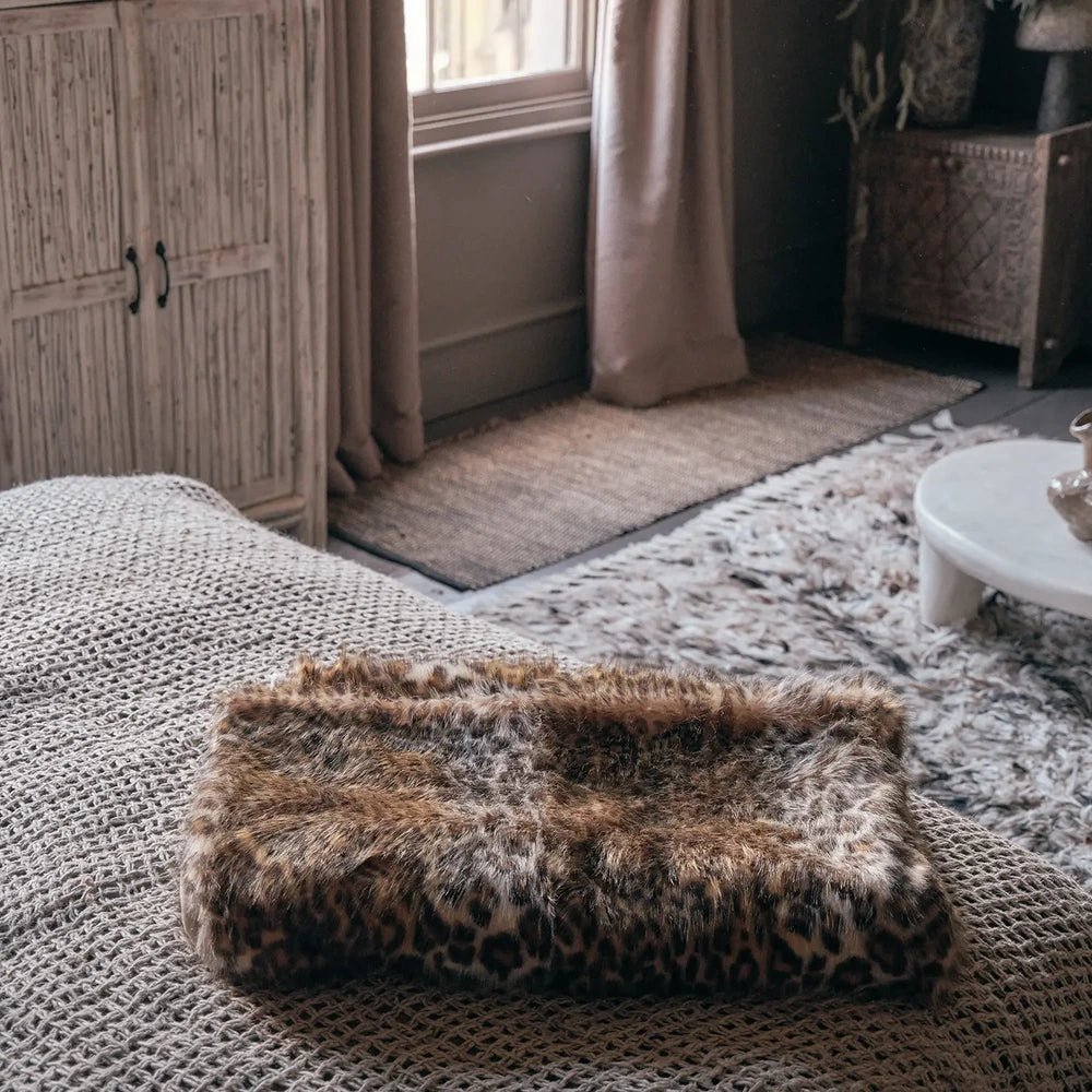 Savannah throw folded on a woven sofa seat, showing its brown and cream animal pattern, soft raised texture and fluffy edge in a neutral living room.