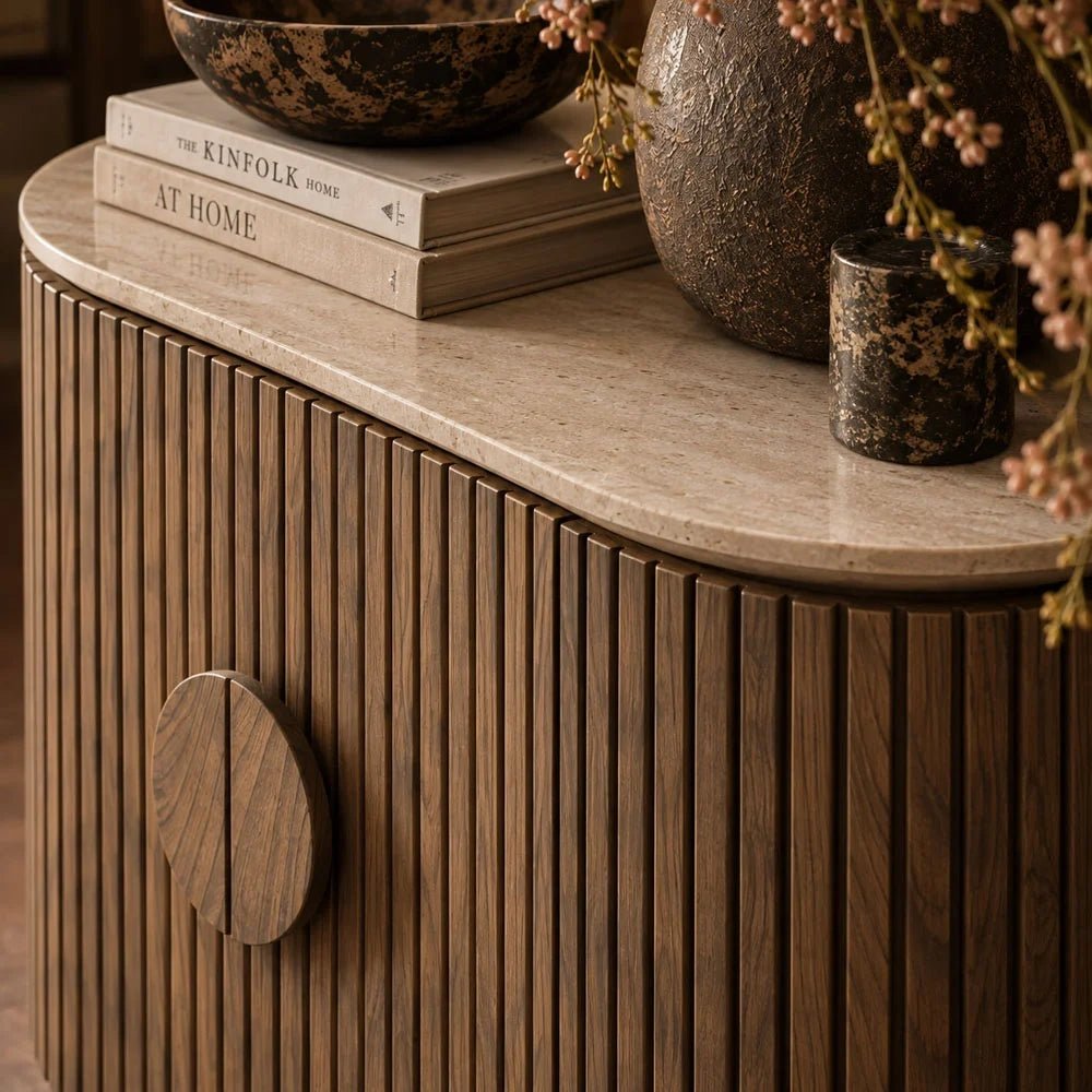 Sheridan wooden cabinet shown close up, revealing narrow vertical slats, a round central handle and a pale rounded top beneath books and decorative vessels.