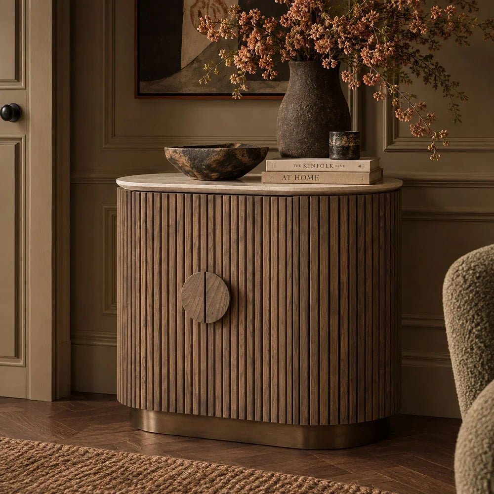 Sheridan wooden cabinet with fluted curved doors and a circular central handle, styled with books, a bowl and a vase of branches against a panelled wall.