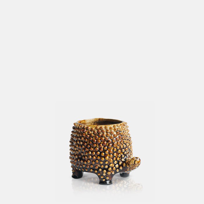 Cutout image on a white background of  a small brown ceramic tortoise pot with  a raised pebble texture.