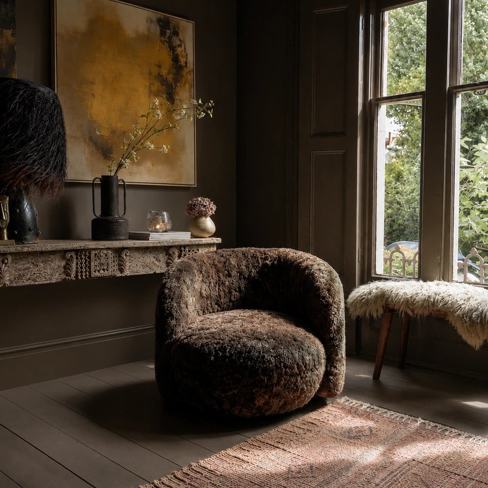 Solstice Canvas Art displayed above a carved console in a dark living room, showing an abstract ochre, cream and black composition beside a textured armchair.