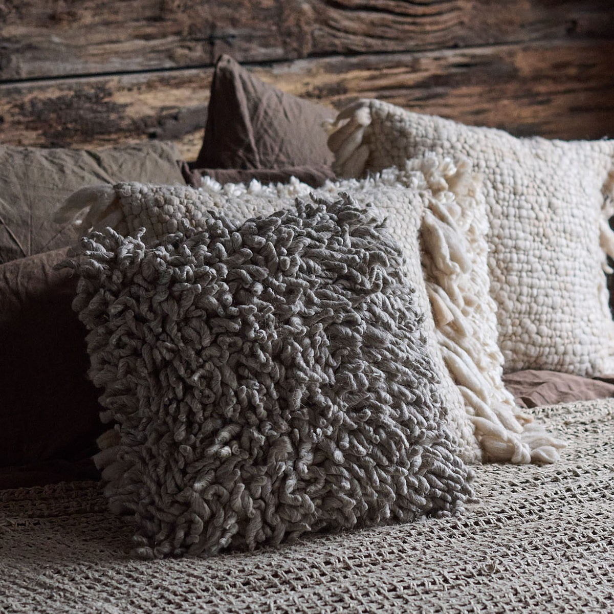 A close-up of a square-shaped cushion with a textured design in a stone color, surrounded by other cushions with different textures and colors in the background.