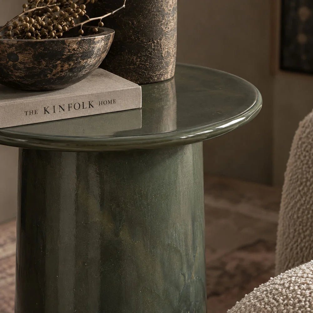 Thayer stoneware side table shown in detail, highlighting the glossy rounded rim and mottled green cylindrical base beneath a dark bowl and stacked book.