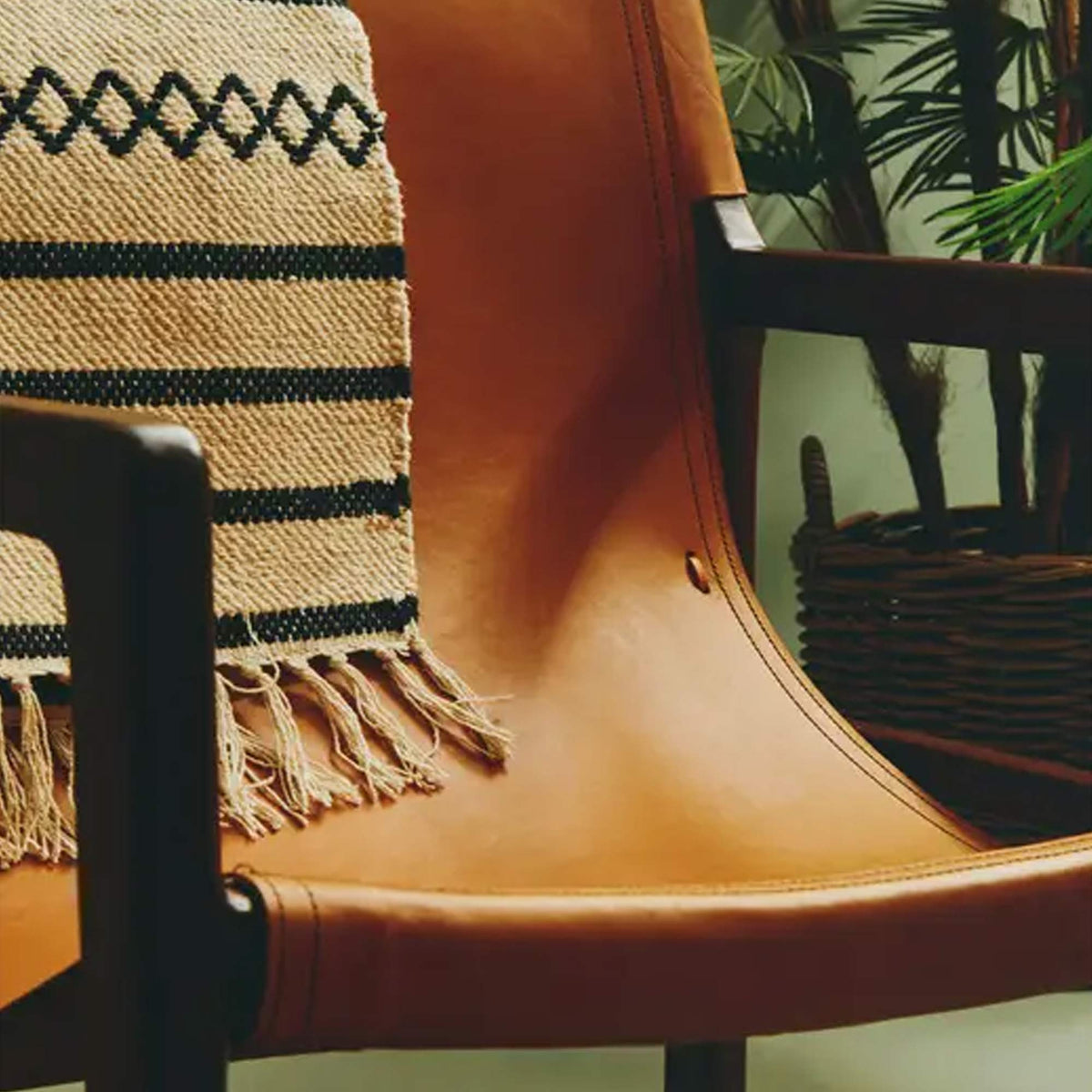 A closeup of the warm brown leather seat of the Tobin Leather Sling Chair, draped with a black and cream striped small rug