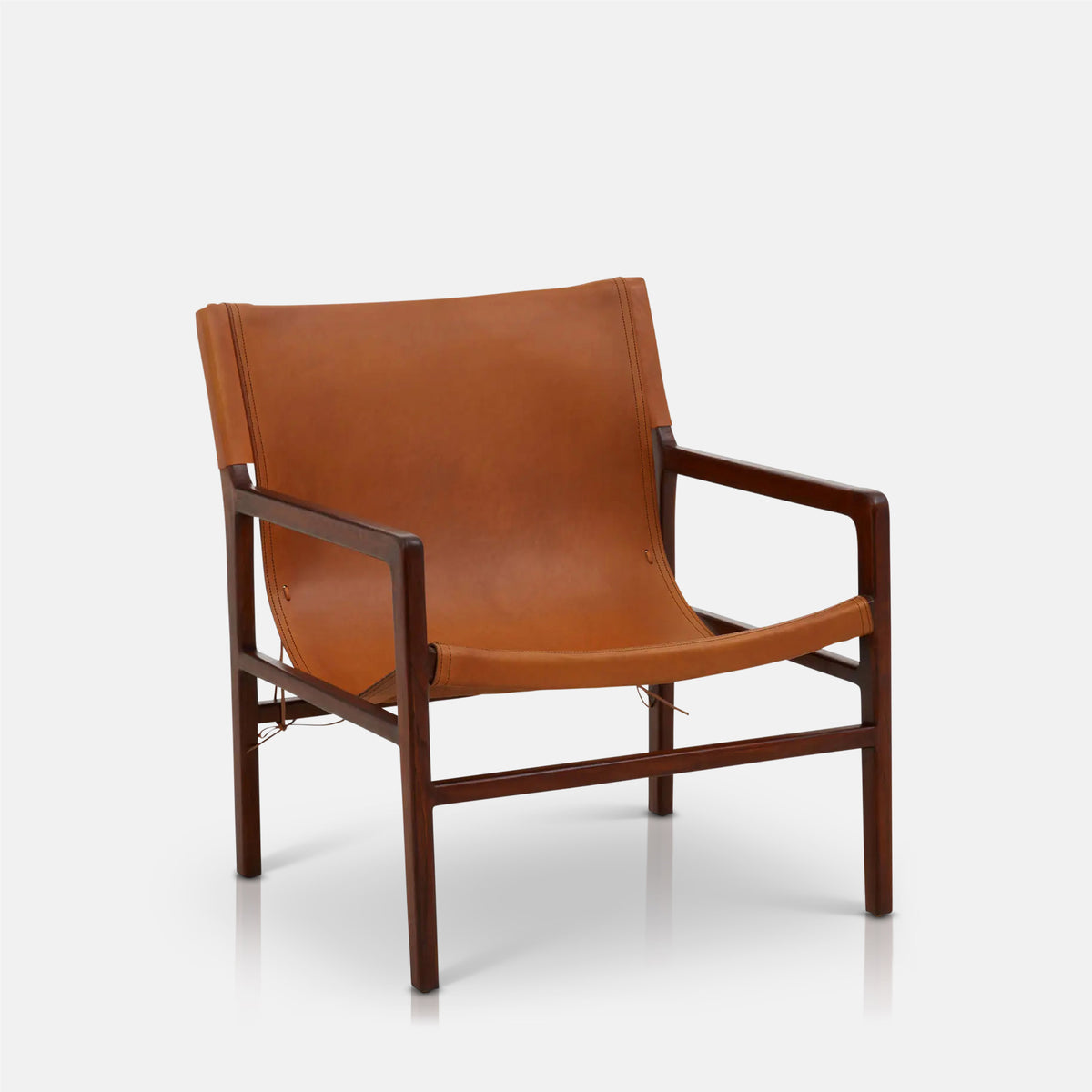 A cutout of the Tobin Leather Sling Chair, a mid-century style low square chair in teakwood with a warm brown leather seat.