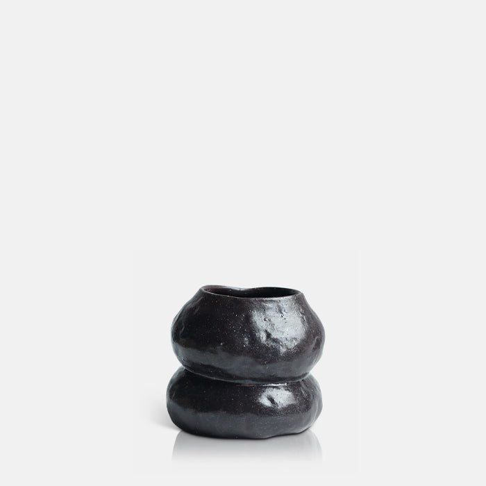 Cutout image on a white background of a small organically curved ceramic vase in a dark brown finish.