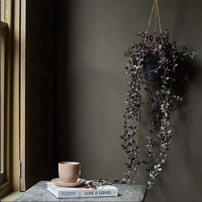 A hanging pot with an artificial trailing plant with purple and green leaves.