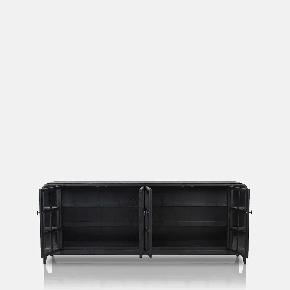 Trumbull wooden sideboard shown with its glazed doors open, revealing dark interior shelves, a long rectangular frame, rounded outer corners and short legs.