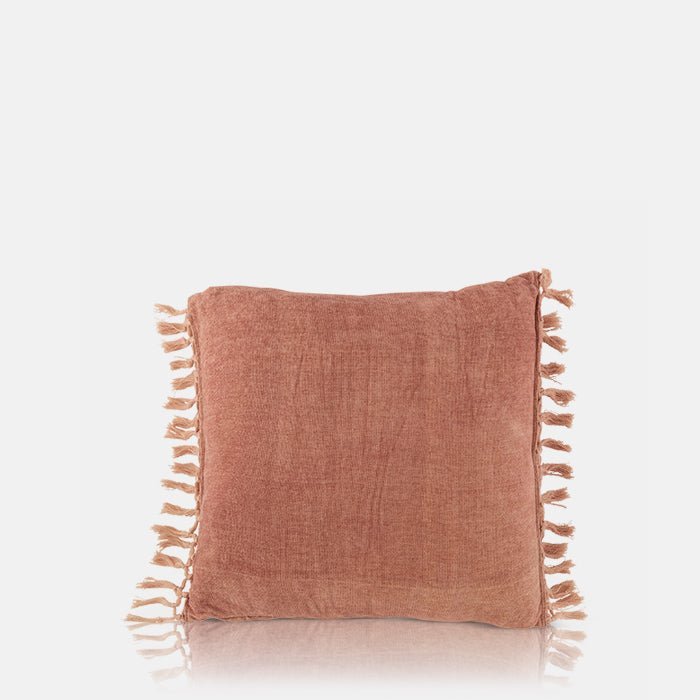 A cutout of the Uvero Cushion, a square fringed cushion in a dusky pink hue.