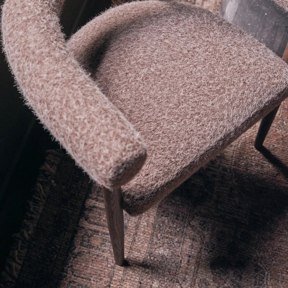 Virgil upholstered dining chair viewed from above, showing its rounded seat, curved padded arm, textured taupe fabric and slim dark legs on a rug.