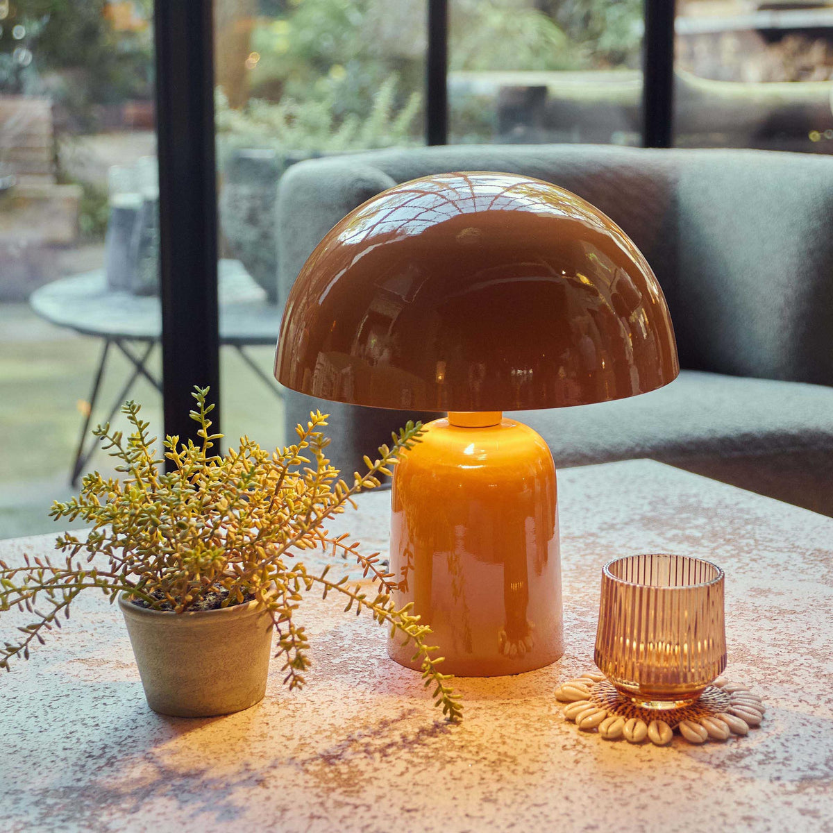 An orange dome table lamp giving off a warm glow on a counter top next to a faux plant and a small glass candle holder.