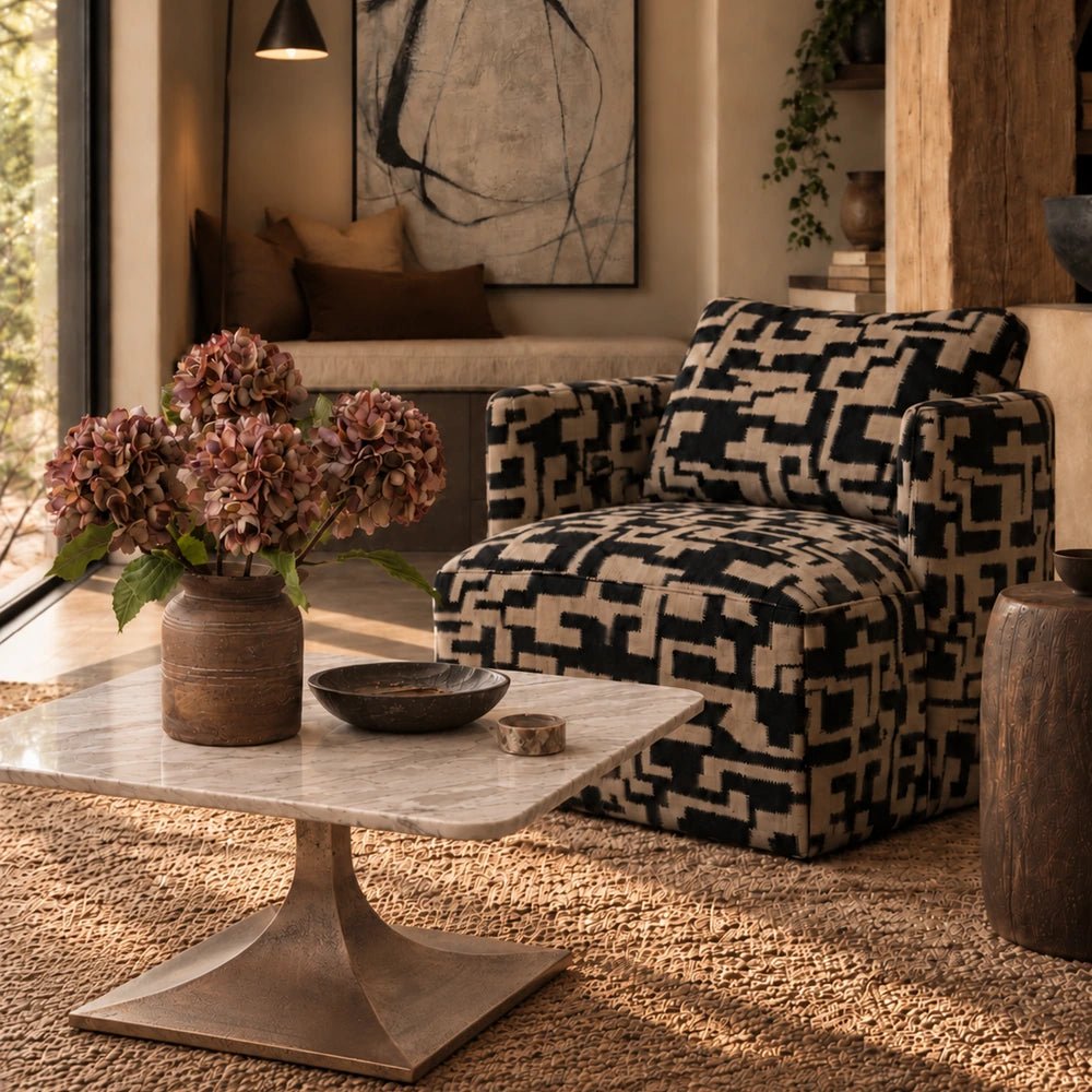Waylon Marble Coffee Table with pale rounded stone top and sculptural base, styled with books and decorative objects in a warm neutral living room.