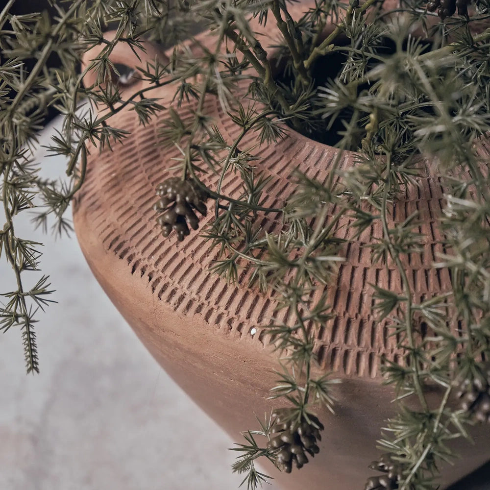 Westbrook ceramic vase shown close up beneath trailing green foliage, highlighting the terracotta surface, rows of vertical indentations and curved shoulder around the opening.