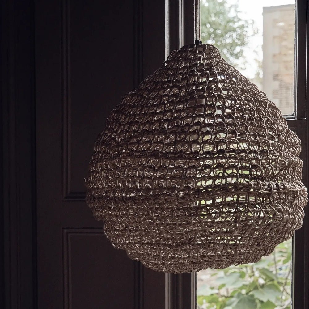 Westcott paper rope pendant beside a window, showing its rounded teardrop shape, open woven texture and natural brown fibres against dark wall panelling.