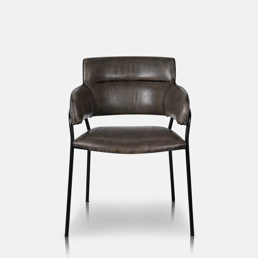 Whitcomb faux leather dining chair shown from the front, with dark padded upholstery, a curved back, cushioned arms and slim black metal legs.