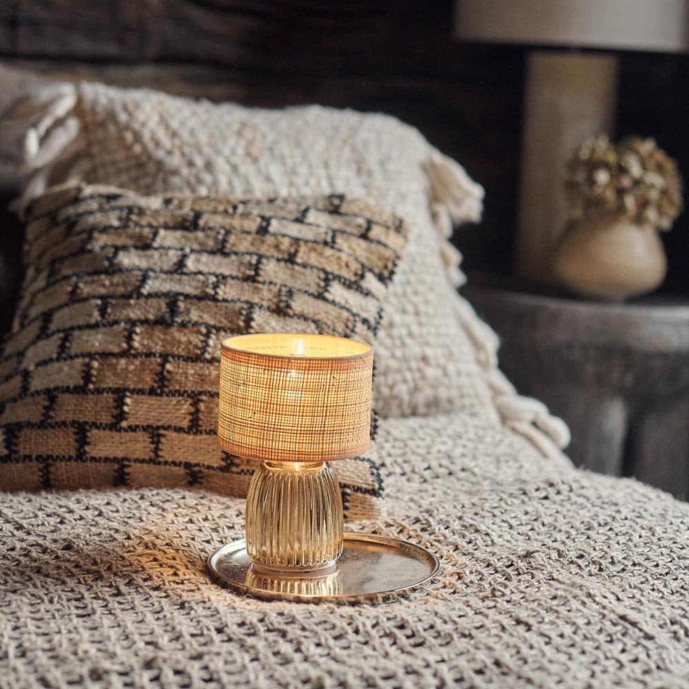 A small portable lamp sitting on a bed in front of a brick patterned cushion.