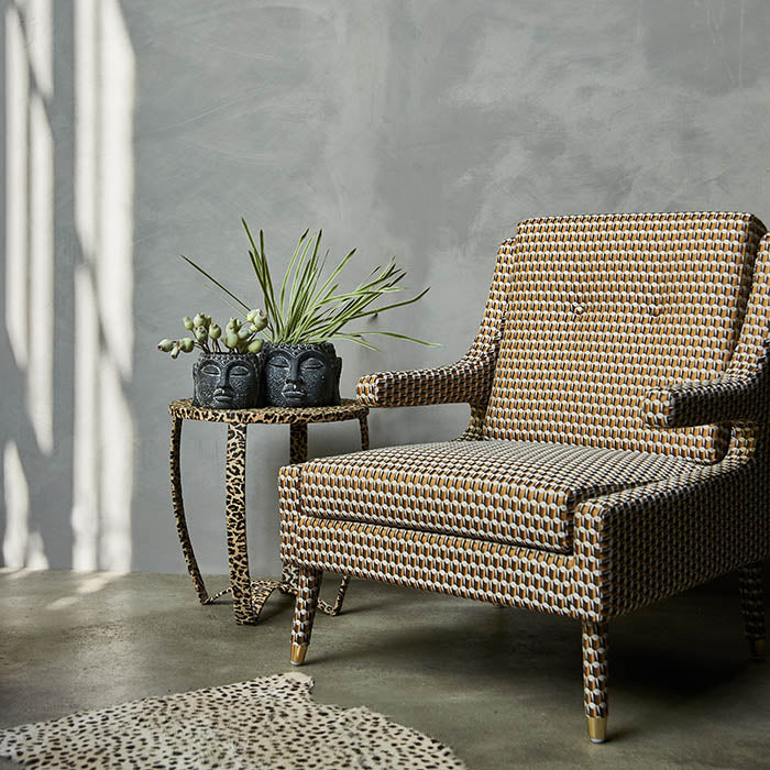 An upholstered orange and brown armchair in an abstract pattern with sculptural armrests and gold metal feet.