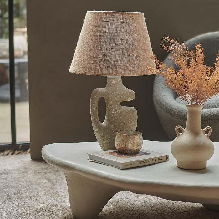 Table lamp with sculptural base in cut-out design and tapered jute lamp shade.