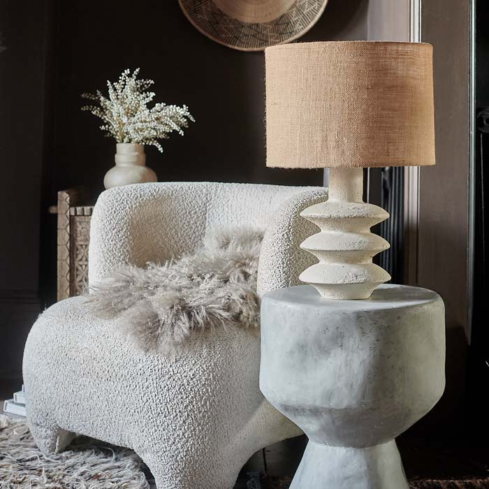 Sculptural white table lamp with jute shade, on stone-look side table.