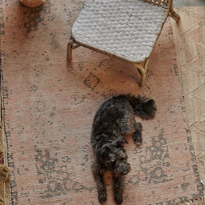 A black dog lies on a woven pink and brown vintage-look jute rug.