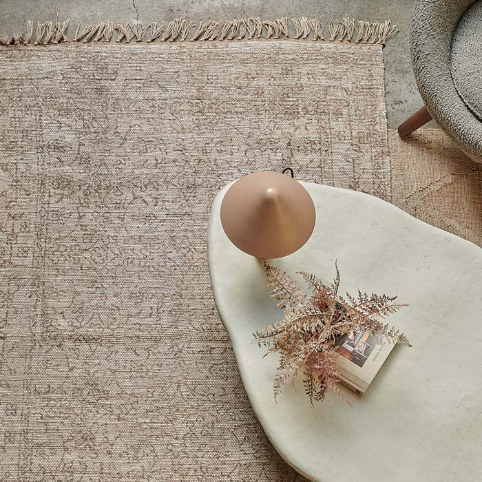 A large woven jute rug with subtle floral pattern design and tassels.