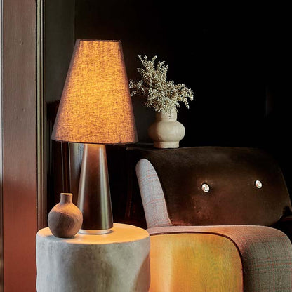 Black table lamp on side table next to armchair, warm light glowing through lamp shade.